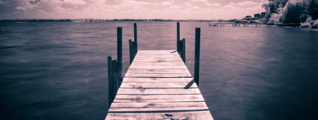 Image of dock in the lake on a cloudy day with a purple and blue hue to it.